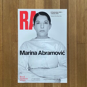 Op de afbeelding: Een poster die reclame maakt voor een tentoonstelling in de Royal Academy of Arts met kunstenaar Marina Abramović. De poster toont een zwart-witfoto van Abramović met de tekst "Marina Abramović" in vetgedrukte, zwarte letters. De poster bevat ook de data "23 september 2023 - 1 januari 2024" en de tekst "Friends of the RA go free".