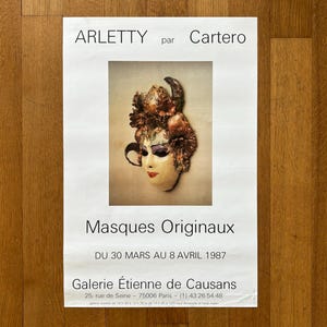 May include: A poster advertising an exhibition of original masks by artist Cartero. The poster features a close-up photograph of a colorful, ornate mask with a female face. The text on the poster reads "ARLETTY par Cartero", "Masques Originaux", "DU 30 MARS AU 8 AVRIL 1987", "Galerie Étienne de Causans", "25, rue de Seine - 75006 Paris - (1) 43.26.54.48", and "galerie ouverte de 10 h 30 à 12 h 30 et de 14 h 30 à 19 h sauf dimanche et jours fériés".