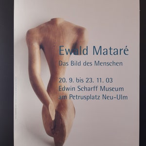May include: A poster advertising an exhibition of sculptures by Ewald Mataré. The poster features a close-up of a wooden sculpture of a human torso. The text on the poster reads "Ewald Mataré, Das Bild des Menschen, 20. 9. bis 23. 11. 03, Edwin Scharff Museum am Petrusplatz Neu-Ulm."