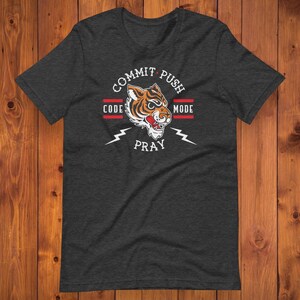 K&ouml;nnte beinhalten: Ein dunkelgraues T-Shirt mit einem Tiger-Motiv und dem Text "Commit Push Code Pray Mode".