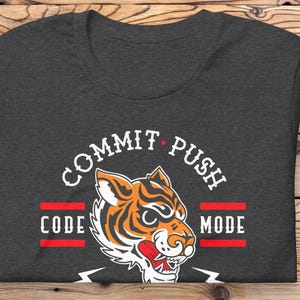 K&ouml;nnte beinhalten: Dunkelgraues T-Shirt mit einem wei&szlig;en Grafikdruck eines Tigers mit dem Text "COMMIT PUSH CODE MODE" drumherum.