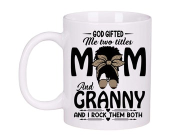 May include: White ceramic mug with a black and brown graphic of a woman with a headband and sunglasses. The text on the mug reads "God gifted me two titles Mom and Granny and I rock them both".