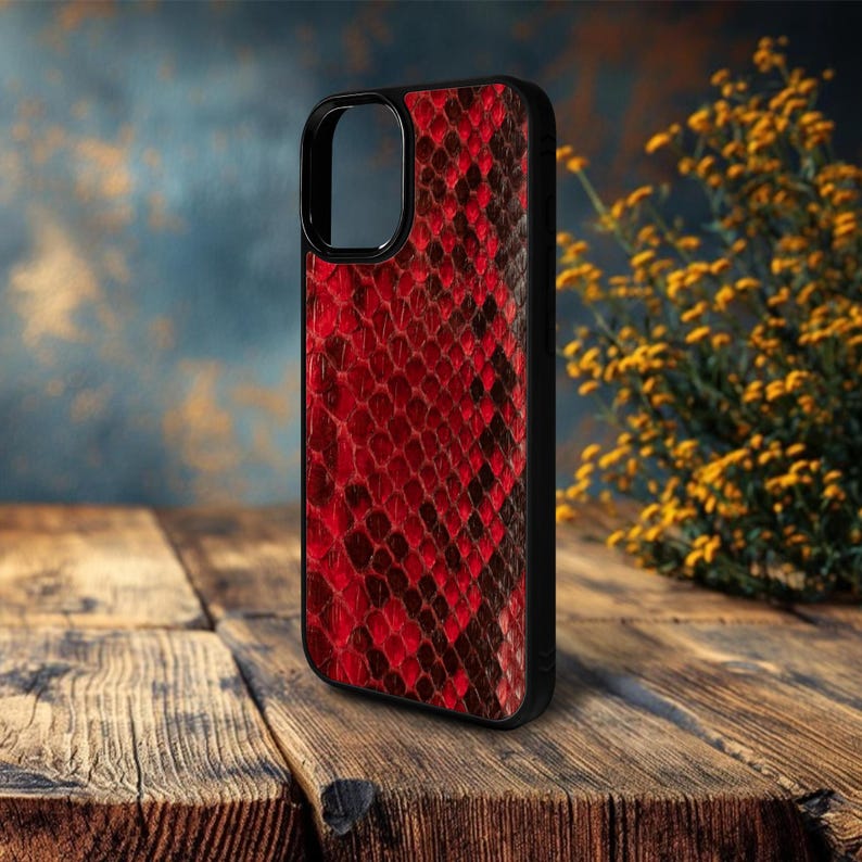 May include: A smartphone case with a red and black snakeskin pattern. The case has a black border and a cutout for the camera. The case is sitting on a wooden surface.