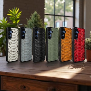 Könnte beinhalten: Sechs Smartphone-Hüllen mit Schlangenmuster in verschiedenen Farben: Weiß, Grau, Schwarz, Grün, Orange und Rot. Die Hüllen sind auf einem Holztisch angeordnet und zeigen ihr strukturiertes Design und ihre schützenden Eigenschaften.