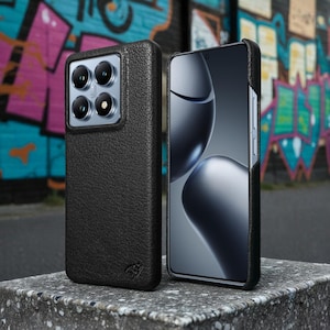 Puede incluir: Funda de teléfono negra texturizada con un recorte cuadrado para la cámara, junto a un smartphone con pantalla curva. La funda tiene un logotipo sutil en la parte inferior. El fondo presenta arte de graffiti colorido.