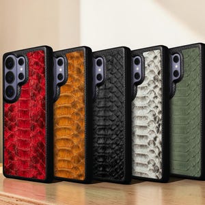 May include: A selection of mobile phone cases in red, orange, black, white, and green. Each case has a textured, snake-skin-like design and a black border. The cases are displayed next to each other.