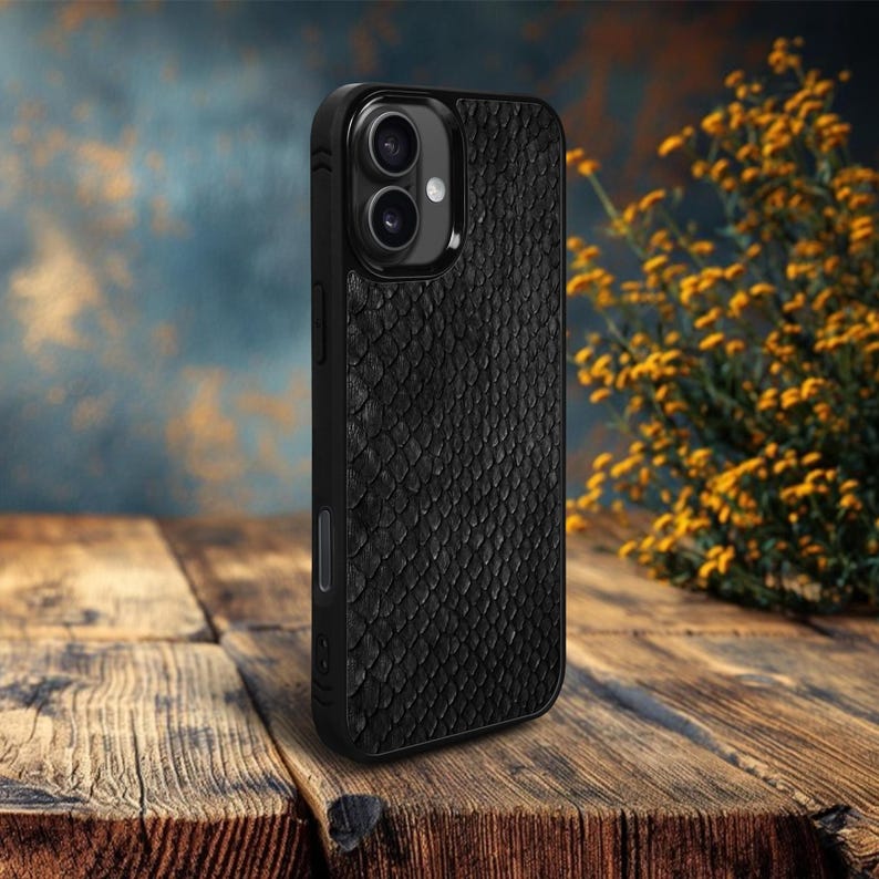 May include: A black phone case with a textured, scale-like pattern. The case has a glossy black camera module and is set against a blurred background and a wooden surface. The case is designed to protect a smartphone.