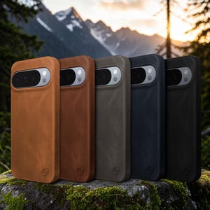 Puede incluir: Una fila de fundas de teléfono de cuero en varios colores: marrón, marrón rojizo, gris, azul marino y negro. Cada funda tiene un recorte para la cámara y un pequeño logotipo en relieve. Las fundas se exhiben sobre una roca cubierta de musgo.