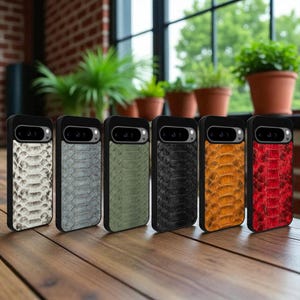 Puede incluir: Una colección de seis fundas para teléfono con textura de piel de serpiente en varios colores: blanco, gris, verde oliva, negro, naranja y rojo. Cada funda tiene un borde negro y un recorte para la cámara. Las fundas se muestran sobre una superficie de madera.