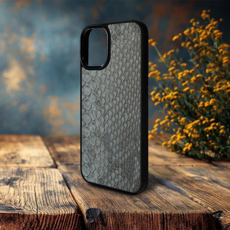 May include: A black smartphone case with a gray snakeskin pattern. The case has a sleek, modern design and is made of a durable material. The case is shown on a wooden surface.