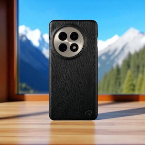 May include: Black leather phone case with a textured surface. The case has a circular camera cutout with four lenses and a silver-colored ring. The background shows a mountain range and a blue sky.