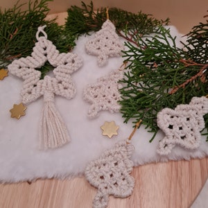 Könnte beinhalten: Ein Set aus fünf handgefertigten Makramee-Weihnachtsanhängern in Cremefarbe. Die Anhänger sind in Form eines Sterns, eines Baumes und eines Herzens. Die Anhänger sind mit goldenem Glitzer verziert.