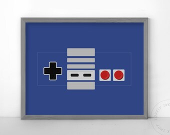 May include: A framed print of a retro video game controller on a blue background. The controller has a black plus sign, two gray buttons, and two red buttons.