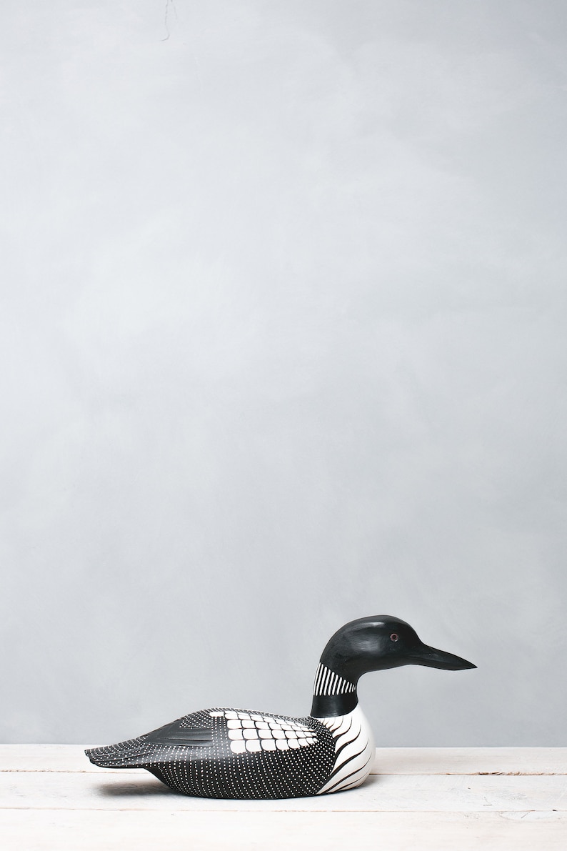 May include: A black and white wooden loon figurine with a red eye. The loon is sitting on a white surface.