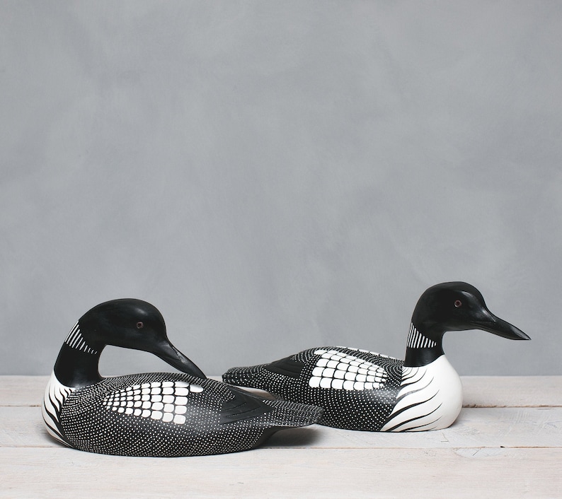Puede incluir: Dos tallas de madera de p&aacute;jaro loon en blanco y negro. El loon de la izquierda est&aacute; mirando hacia la derecha y el loon de la derecha est&aacute; mirando hacia la izquierda. Ambos loons tienen ojos negros y marcas blancas.
