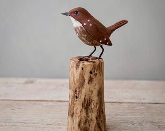 Könnte beinhalten: Eine handgeschnitzte Holzvogelfigur, braun und weiß bemalt, auf einem Holzstumpf sitzend. Der Vogel hat einen langen, dünnen Schnabel und kleine, schwarze Augen.