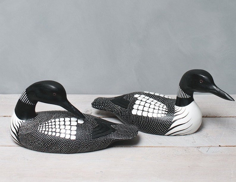 May include: Two black and white wooden loon bird carvings. The birds are painted with a black and white geometric pattern. The birds are facing different directions.