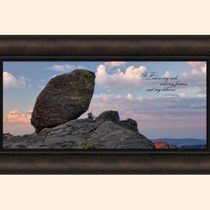 May include: A framed print with a scenic landscape of a large rock formation in a mountainous area. The sky is a vibrant blue with fluffy white clouds. The text "The Lord is my rock, and my fortress, and my deliverer." is printed on the image. The scripture reference "2 Samuel 22:2" is also printed on the image.