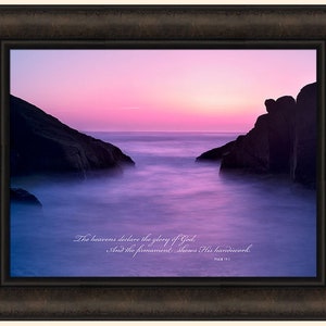 May include: A framed print with a photograph of a pink and purple sunset over the ocean. The water is calm and the sky is filled with color. The text "The heavens declare the glory of God. And the firmament shows His handiwork. Psalm 19:1" is printed below the image.
