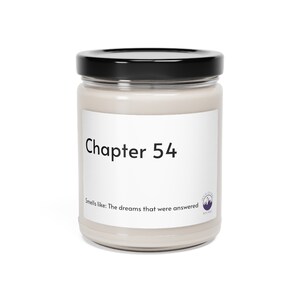 May include: A candle in a clear glass jar with a black lid. The label reads "Chapter 54" above the text "Smells like: The dreams that were answered". A small purple mountain logo is on the bottom right.