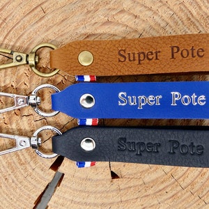 Peut inclure: Trois porte-clés en cuir marron, bleu et noir, chacun avec un mousqueton en métal. Les porte-clés sont estampés des mots "Super Pote" et d'une étoile. Les porte-clés bleus et noirs ont un petit ruban tricolore.