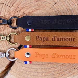 Peut inclure: Trois porte-clés en cuir noir, marron et orange, chacun avec un mousqueton en métal. Les porte-clés sont estampillés des mots "Papa d'amour" et d'un symbole de cœur. Chaque porte-clés a un petit ruban tricolore français.