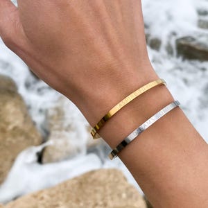Puede incluir: Dos pulseras de oro y plata con mensajes inspiradores grabados. La pulsera de oro dice "ASPIRE TO INSPIRE" y la pulsera de plata dice "DREAMS COME TRUE".