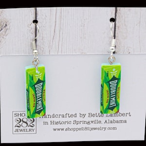 May include: A pair of novelty earrings featuring a miniature replica of a Doublemint gum pack. The earrings are green and white with the text "DOUBLEMINT" and silver-colored ear wires. The earrings are displayed on a white card.