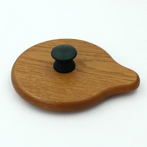 May include: A wooden lid with a black knob. The lid is shaped like a teardrop and has a smooth, polished finish.