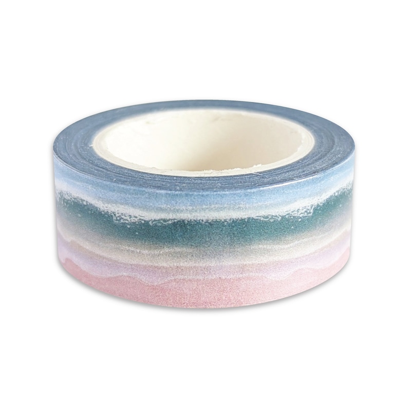 May include: A roll of decorative washi tape with a gradient design. The tape transitions from a light pink at the bottom to a teal green, light blue, and finally a dark blue at the top. The tape is on a white background.