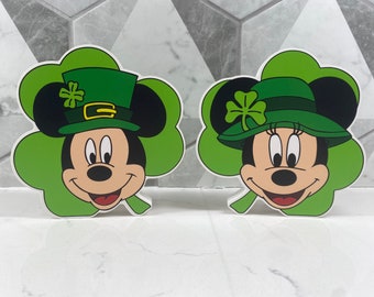 May include: Two green shamrock-shaped decorations featuring Mickey Mouse and Minnie Mouse wearing green hats with shamrock accents.