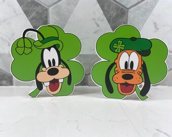 May include: Two green shamrock-shaped cutouts with cartoon faces of Goofy and Pluto wearing green hats with shamrocks.