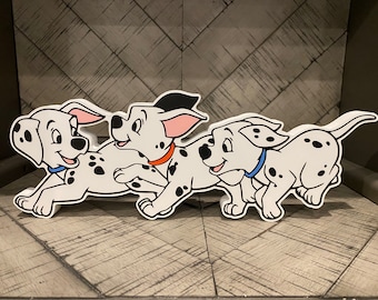 May include: Three white Dalmatian puppies with black spots are running. The puppy in the middle has a red collar, the puppy on the left has a blue collar, and the puppy on the right has a blue collar.