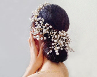 May include: A gold and white pearl hairpiece with a delicate vine design. The hairpiece is worn by a person with dark hair, but the person's face is not visible.