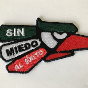 May include: A black and red embroidered patch with a stylized eagle design. The eagle has a green head and white eyes. The patch has the words "SIN MIEDO AL ÉXITO" written on it.