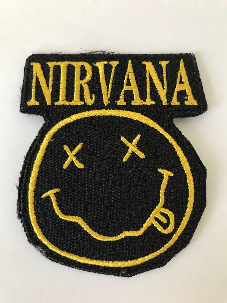 Peut inclure: Un patch brod&eacute; noir et jaune avec le mot "NIRVANA" en lettres jaunes au-dessus d'un smiley jaune avec deux X noirs pour les yeux.