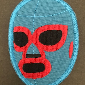 Puede incluir: Un parche de tela azul con un diseño de máscara de lucha libre roja y negra. La máscara tiene una nariz roja y ojos con contornos negros.
