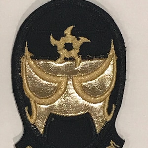 以下が含まれることがあります： 星形のデザインが施された、スタイリッシュなレスリングマスクが刺繍された黒と金のワッペン。ワッペンは黒の背景に金のステッチと中央に金の星形のデザインが施されています。マスクは金で縁取られ、中央に金の星形のデザインが施されています。ワッペンは直径約5cmです。