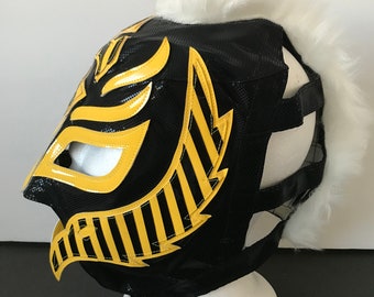 Può includere: Maschera da wrestling nera con accenti gialli e bianchi. La maschera ha un bordo di pelliccia bianca intorno alla parte superiore.