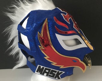 Può includere: Maschera da wrestling blu e bianca con un design di aquila rosso e oro. La maschera ha un bordo in pelliccia bianca e la parola "MASK" è stampata in basso.