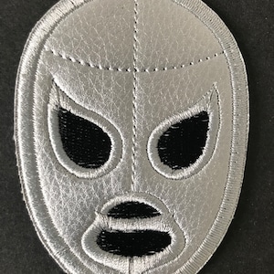 Puede incluir: Un parche bordado de máscara de lucha libre plateado y negro. La máscara tiene un diseño tradicional de luchador con fondo plateado y ojos, boca y nariz negros.