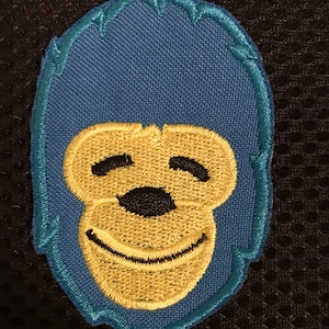 May include: An embroidered patch featuring a smiling monkey face in blue and yellow.