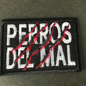 May include: White embroidered patch with the text "PERROS DEL MAL" in white with red scratch marks over the text on a black background.