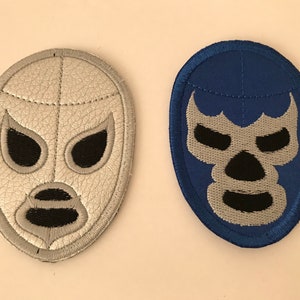 以下が含まれることがあります： 黒い目の穴と黒い口のある、銀色のマスクと青いマスクの2つのレスリングマスク。マスクは白いステッチで刺繍されています。