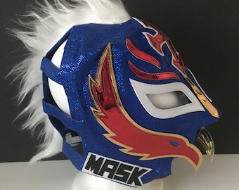 Può includere: Maschera da wrestling blu e bianca con un design di aquila rosso e oro. La maschera ha un bordo in pelliccia bianca e la parola "MASK" è stampata in basso.