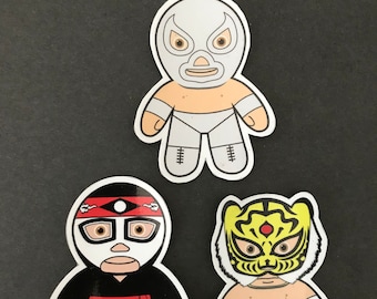 May include: Three colorful wrestler stickers with white outlines. The stickers feature a white masked wrestler, a black masked wrestler with a red headband, and a yellow masked wrestler with a tiger design.
