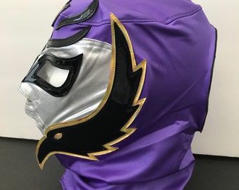 Può includere: Una maschera da wrestling viola con un designo di aquila nero e oro. La maschera ha un viso argentato con buchi neri per gli occhi.