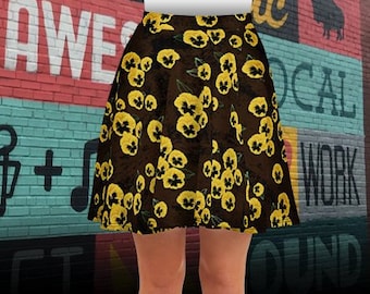 Op de afbeelding: A-lijn rok met een donkerbruine achtergrond en een patroon van gele viooltjes. De rok wordt gedragen met witte schoenen. De achtergrond heeft kleurrijke graffiti-kunst.