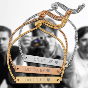 Puede incluir: Tres pulseras ajustables con cadenas de caja en tonos plata, oro rosa y oro. Cada pulsera presenta una barra metálica rectangular grabada con el texto DO. GO. BE. seguido de un símbolo de corazón, asegurada con un cierre de cuenta deslizante.
