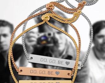 Op de afbeelding: Drie verstelbare schuifarmbanden met boxkettingen in zilver-, roségoud- en goudtinten. Elke armband heeft een rechthoekige metalen staaf gegraveerd met de tekst DO. GO. BE. gevolgd door een hartsymbool, vastgezet met een schuifkraalsluiting.